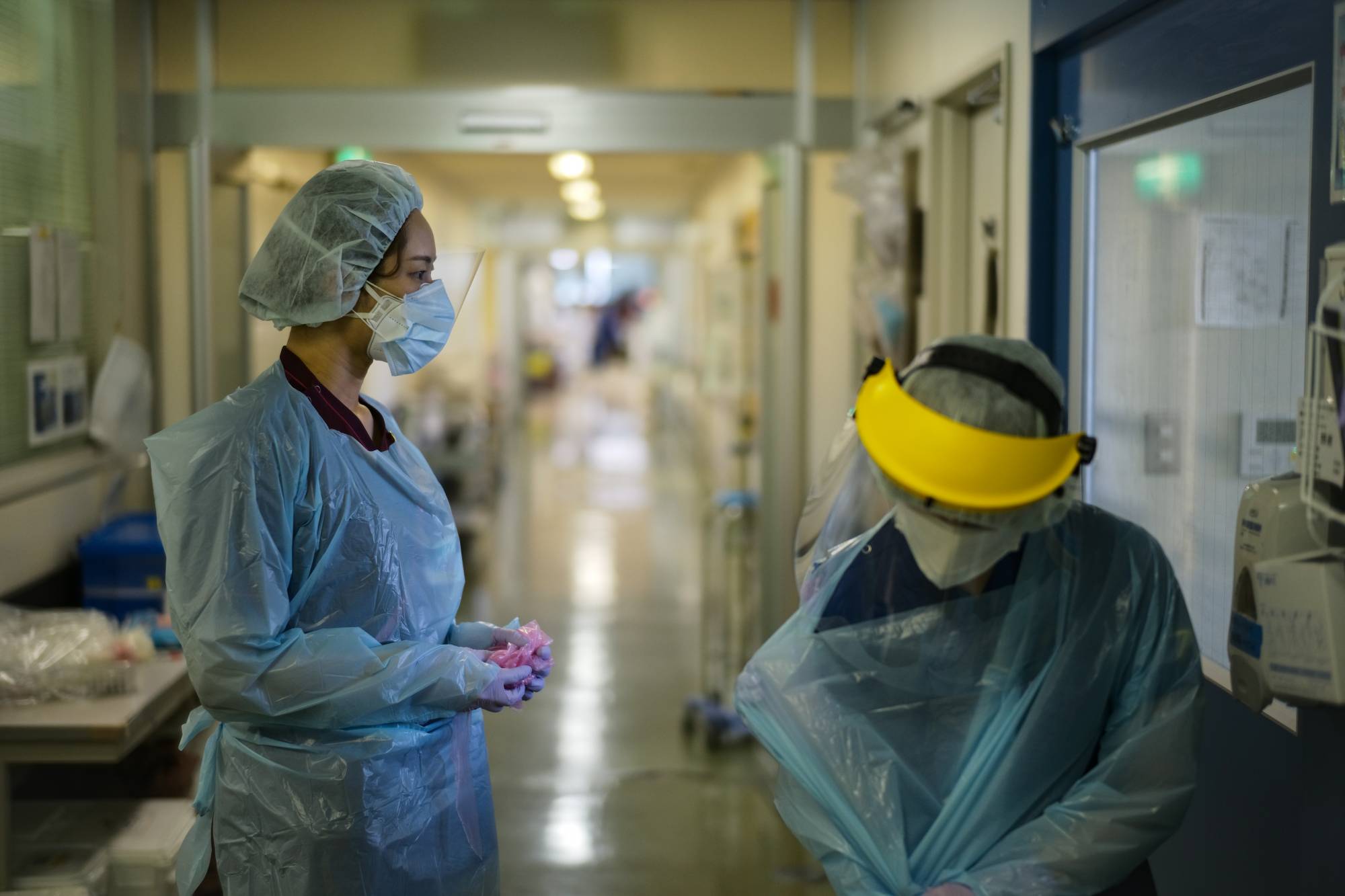 Nao Watarumi (left) waits to remove her protective gear as Junko Yamaguchi does so after emerging from the room of a severely ill COVID-19 patient in the intensive care unit of Itabashi Hospital. | Ryusei Takahashi 