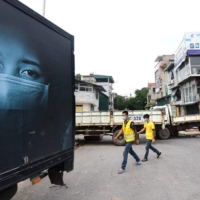 Local residents walk past a make-shift barricade of parked trucks to stop unauthorized travel in Hanoi on July 30 amid a government-imposed two-week lockdown to stop the spread of the coronavirus. | AFP-JIJI