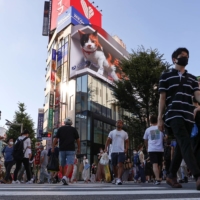 People walk through the Shinjuku district in Tokyo on Sunday. The current surge in COVID-19 cases has forced policymakers to re-examine whether current measures are sufficient to protect public health. | REUTERS