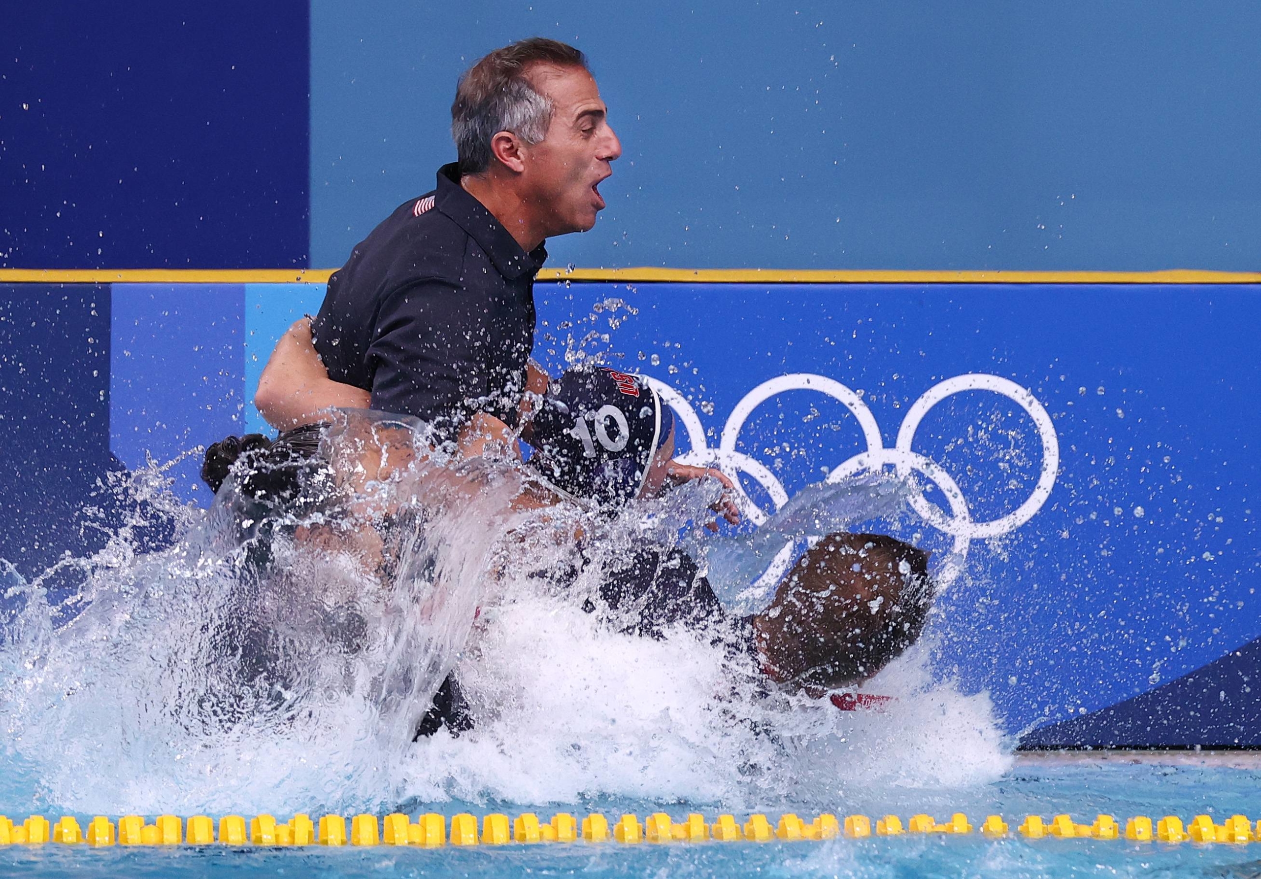 United States' head coach Adam Krikorian is pulled into the pool by team members after they won their match again Spain in the gold medal match of women's water polo. | REUTERS