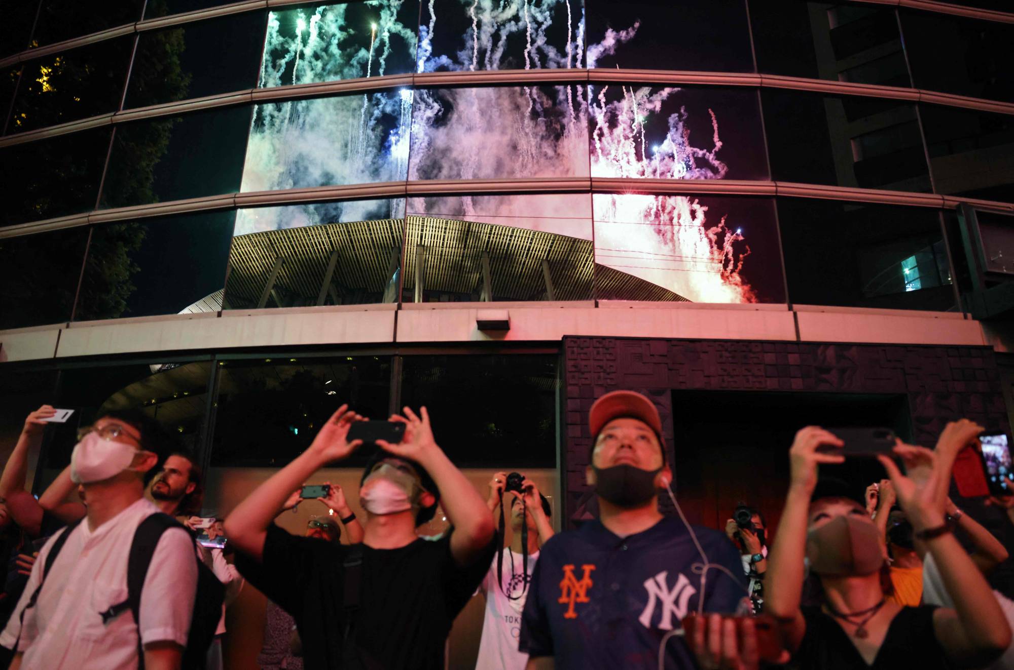 People outside the venue watch as fireworks light up the sky over the National Stadium during the closing ceremony of the Tokyo 2020 Olympic Games. | AFP-JIJI