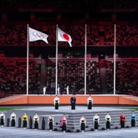 Performers sing the Japanese national anthem as the Olympic flag and Japan\'s flag are raised during the closing ceremony of the Tokyo 2020 Olympic Games. | AFP-JIJI