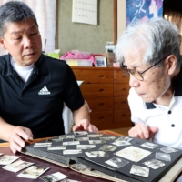 Okiharu Terao (right) and his son Toshiya turn a page of the album containing photos taken by the former\'s father, Motoichi Terao, before the war. | CHUGOKU SHIMBUN
