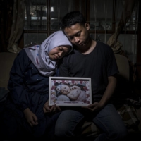 Debiyantoro (left) and Siti Halimah Puspita Sari hold a portrait of their daughter, Alesha Kimi Pramudita, who died from COVID-19 at 22 months old, in Yogyakarta, Indonesia, on July 31. The disease kills far more children in developing countries than in rich ones, and some factors make them especially vulnerable in Indonesia. | ULET IFANSASTI/THE NEW YORK TIMES