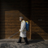 A worker sprays disinfectant as part of routine work to prevent the spread of COVID-19 at a shopping area in Beijing on Friday.  | GETTY IMAGES / VIA BLOOMBERG 