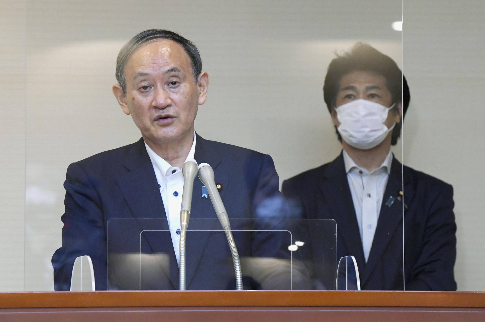 Prime Minister Yoshihide Suga speaks to reporters in Tokyo on Monday, as health minister Norihisa Tamura stands behind him. | POOL / VIA KYODO
