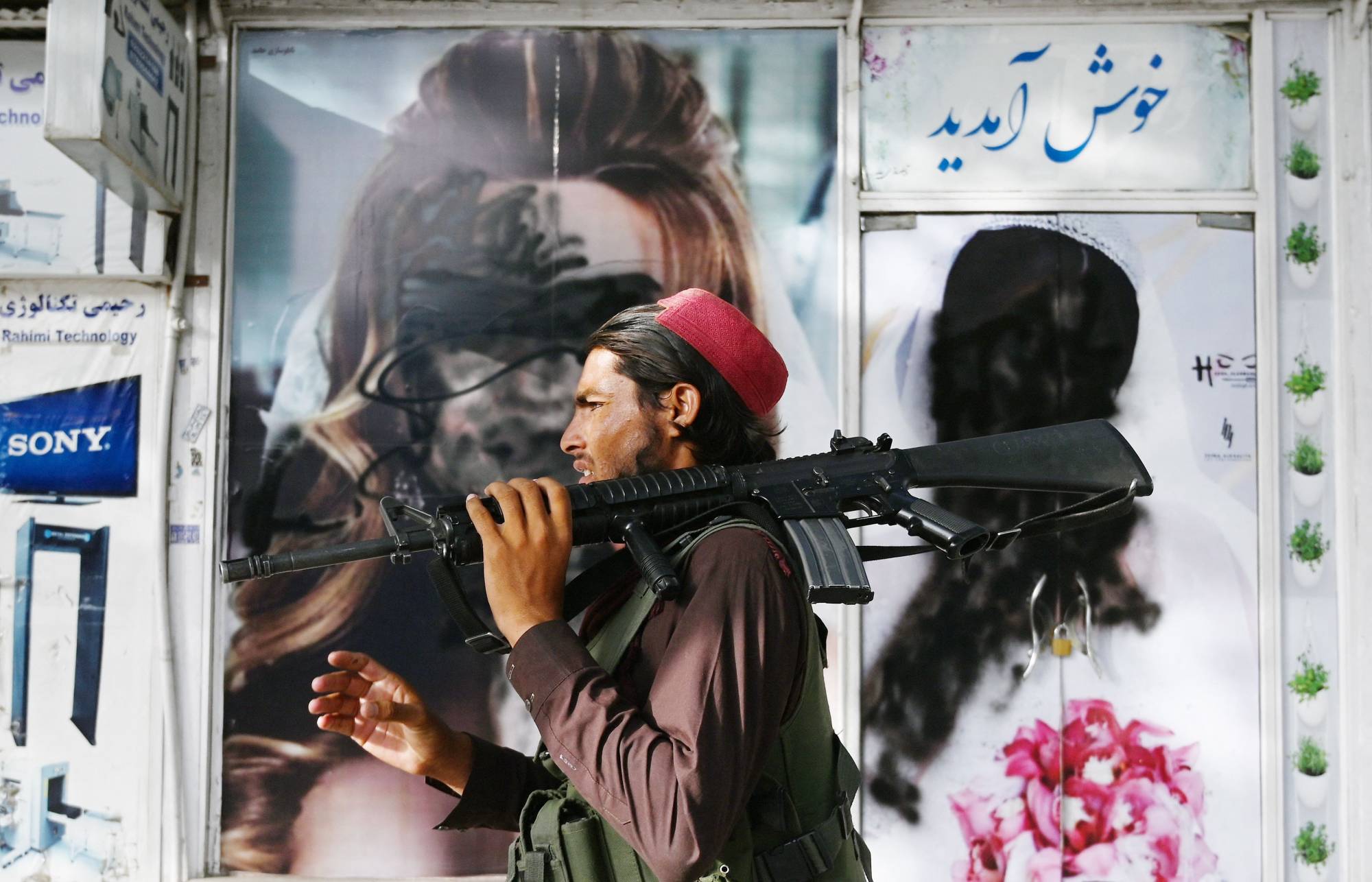 A Taliban fighter on Wednesday walks past a beauty salon in Kabul with images of women defaced using spray paint. | AFP-JIJI