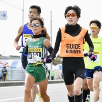 Visually impaired athletes run with a guide. The guide runs alongside the athlete, holding one end of a rope with a loop that is called a tether. The visually impaired person holds the other end of the rope and keeps pace. | KYODO