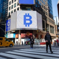 Monitors display Coinbase and Bitcoin signage during the company\'s initial public offering at the Nasdaq MarketSite in New York on April 14. | BLOOMBERG