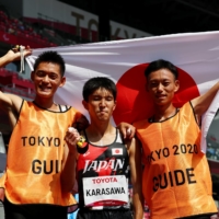 Kenya Karasawa (center) celebrates after winning silver, alongside guides Hiroaki Mogi and Koji Kobayashi.  | REUTERS
