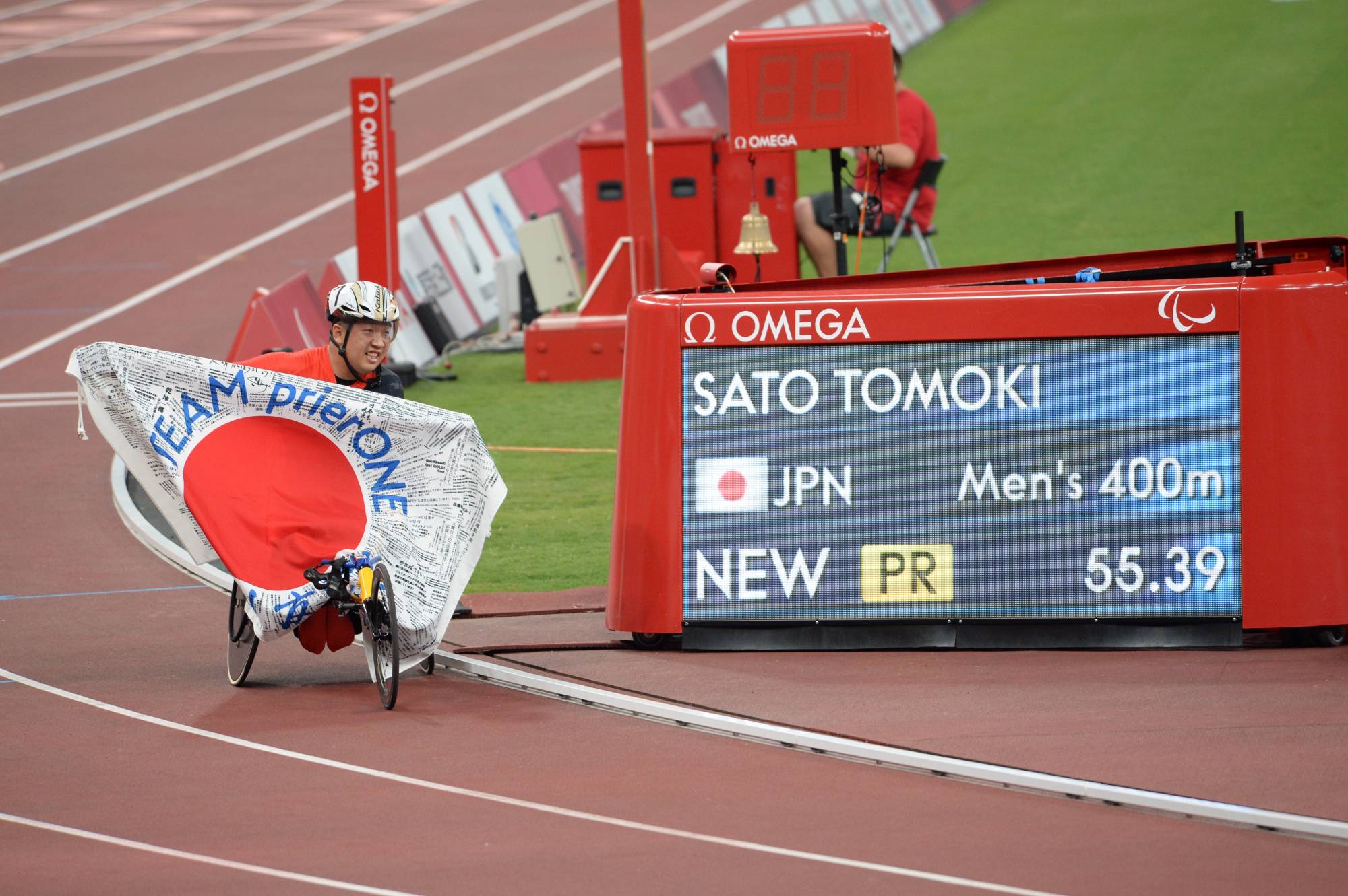 Tomoki Sato poses next to a monitor Friday showing his Paralympic record time of 55.39 seconds in the men's T52 400 meters | DAN ORLOWITZ