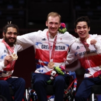 Athletes of Team Great Britain — Dimitri Coutya, Oliver Lam-Watson and Piers Gilliver — celebrate at the medal ceremony for the men\'s epee team wheelchair fencing. | REUTERS