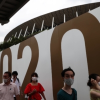 People wearing protective masks walk past the National Stadium, the main venue of the Tokyo 2020 Paralympic Games. | REUTERS