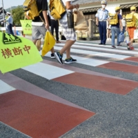 Children Monday walk on a crosswalk that appears to be floating in the air to catch the attention of drivers in front of Chiyokawa Elementary School in Kameoka, Kyoto Prefecture. | KYODO
