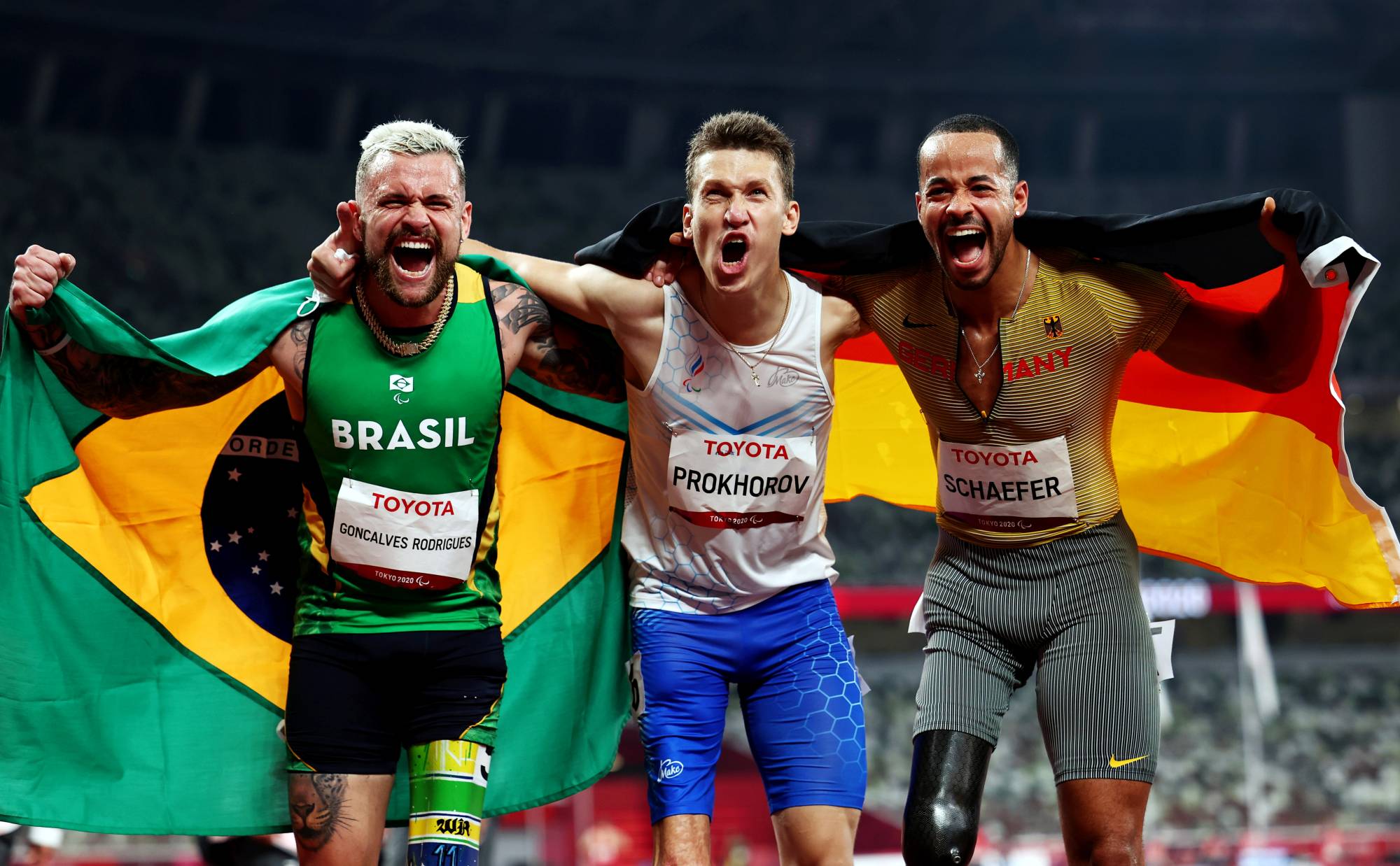 Silver medalist Vinicius Goncalves Rodrigues of Brazil, gold medalist Anton Prokhorov of the Russian Paralympic Committee and bronze medalist Leon Schaefer of Germany celebrate after competing in the men's T63 100 meters. | REUTERS