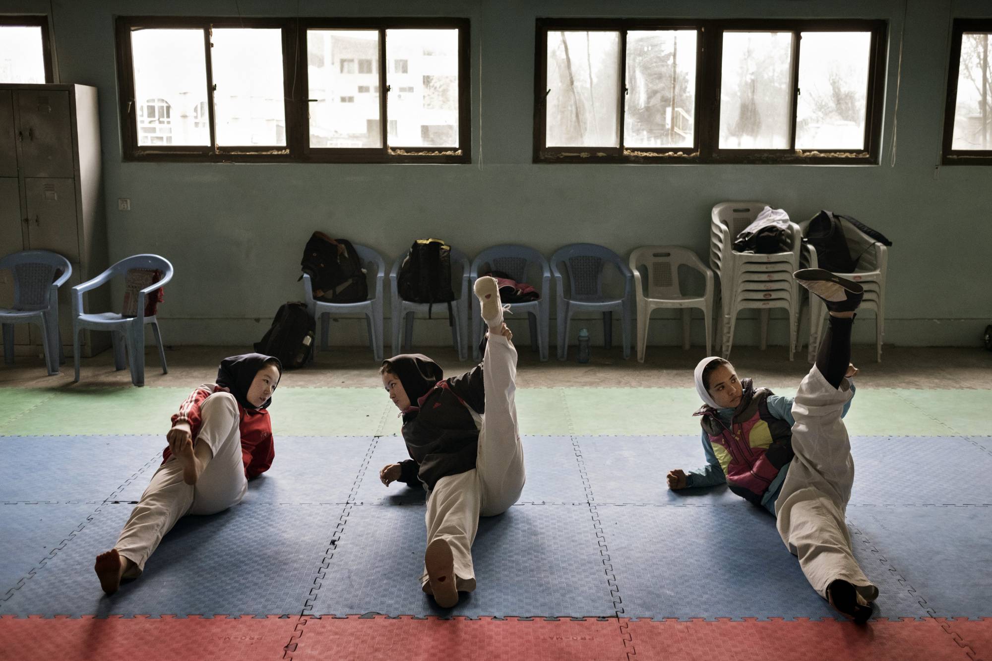 Zakia Khudadadi (left) stretches before training at the Afghan National Taekwondo Federation gym in Kabul in March 2016. | Adam Ferguson / The New York Times