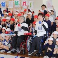 Hidetaka Sugimura (right) and Takayuki Hirose, who competed on Japan\'s silver medal-winning mixed boccia team at the 2016 Paralympics, pose with students at Ariake Nishi Gakuen, an elementary and middle school, in Tokyo on Friday.  | KYODO
