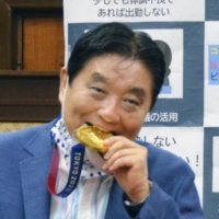 Nagoya Mayor Takashi Kawamura bites the gold medal belonging to softball athlete Miu Goto during a ceremony in Nagoya o Aug. 4. | KYODO