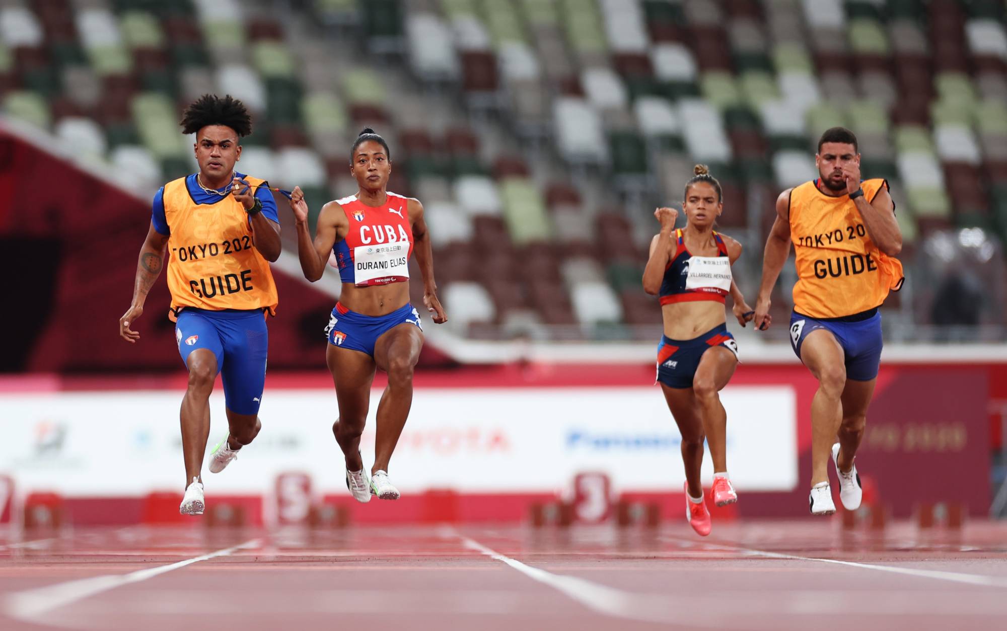 Cuba's Omara Durand Elias, with her guide Yuniol Kindelan Vargas, and Venezuela's Greilyz Greim Villarroel Hernandez, with her guide Edicson Roberto Medina Ramirez, compete in the women's T12 100-meters semifinals. | REUTERS