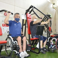 Masaru Taniuchi (left) visits the Saitama Rehabilitation Center in Ageo, Saitama Prefecture, once a week to exercise. | KYODO