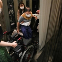 Yuto Hirano, a volunteer for the Paralympics, transfers from his wheelchair for a haircut in Tokyo on Aug. 23. Tokyo improved its infrastructure before the delayed 2020 Games, but activists wonder how long the focus will continue in a country with a long history of excluding people with disabilities.  | CHANG W. LEE/THE NEW YORK TIMES