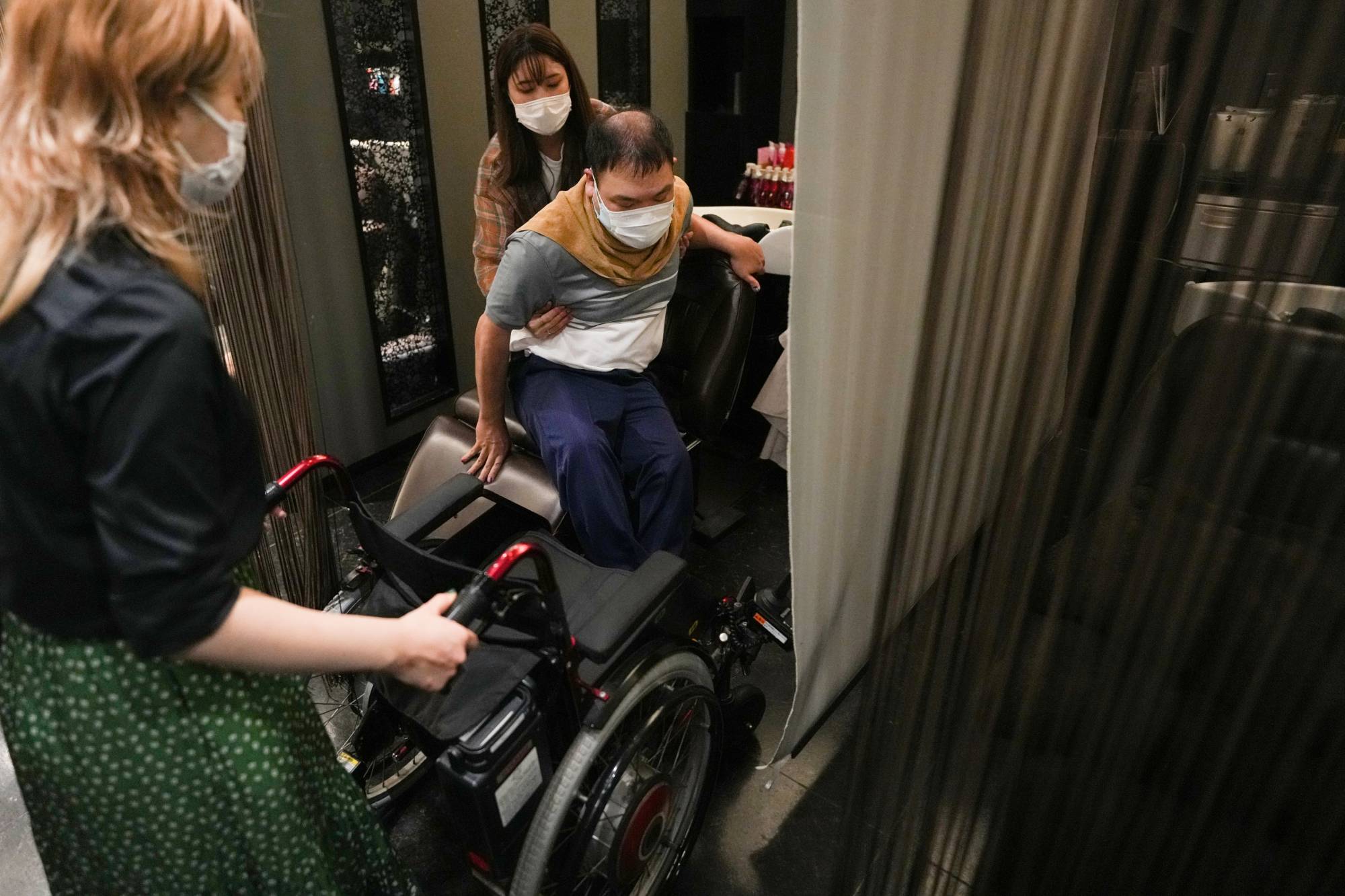 Yuto Hirano, a volunteer for the Paralympics, transfers from his wheelchair for a haircut in Tokyo on Aug. 23. Tokyo improved its infrastructure before the delayed 2020 Games, but activists wonder how long the focus will continue in a country with a long history of excluding people with disabilities. | Chang W. Lee/The New York Times