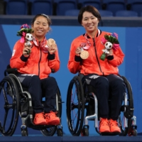 Women\'s doubles bronze medalists Yui Kamiji and Momoko Ohtani celebrate on the podium. | REUTERS