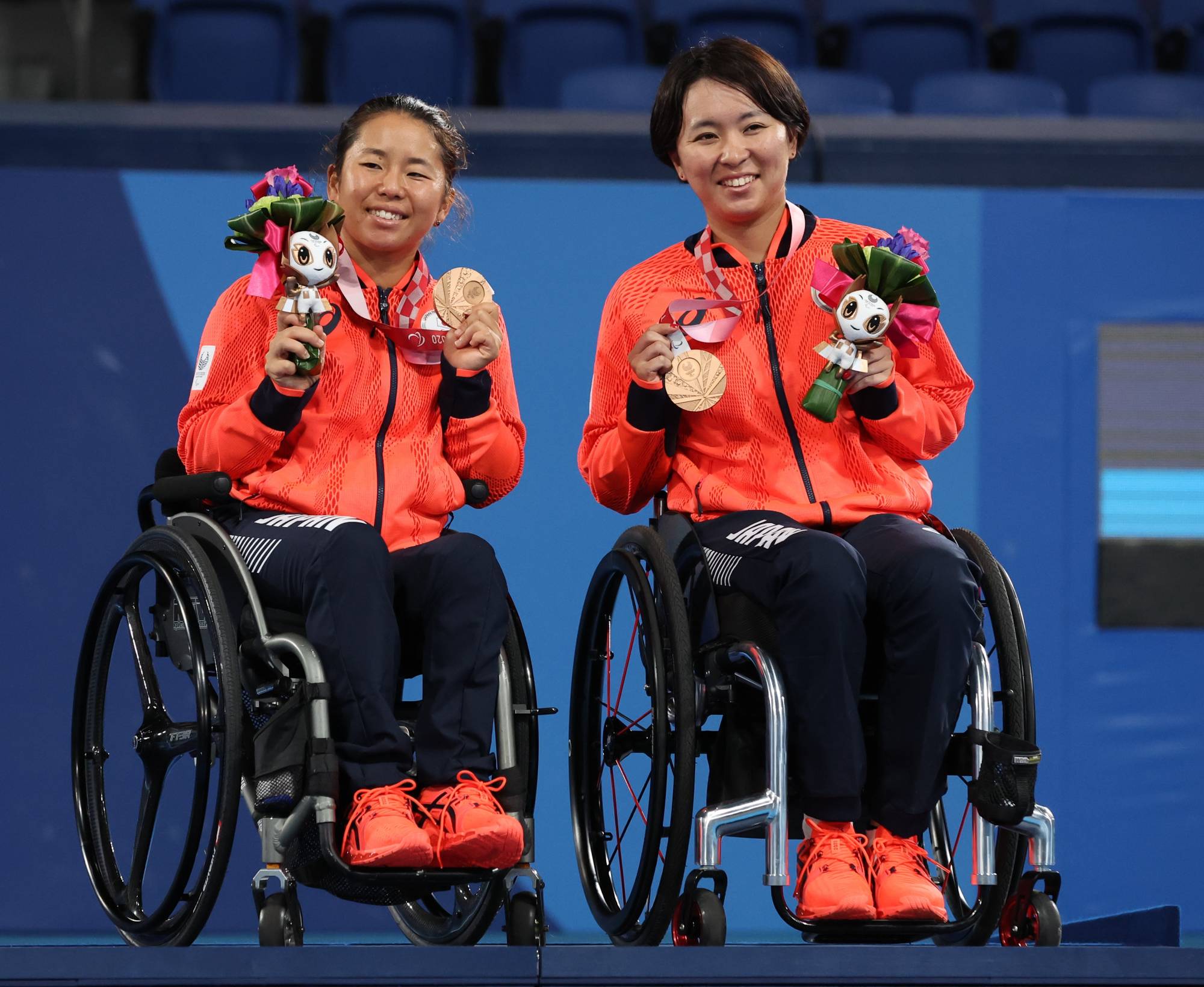Women's doubles bronze medalists Yui Kamiji and Momoko Ohtani celebrate on the podium. | Reuters