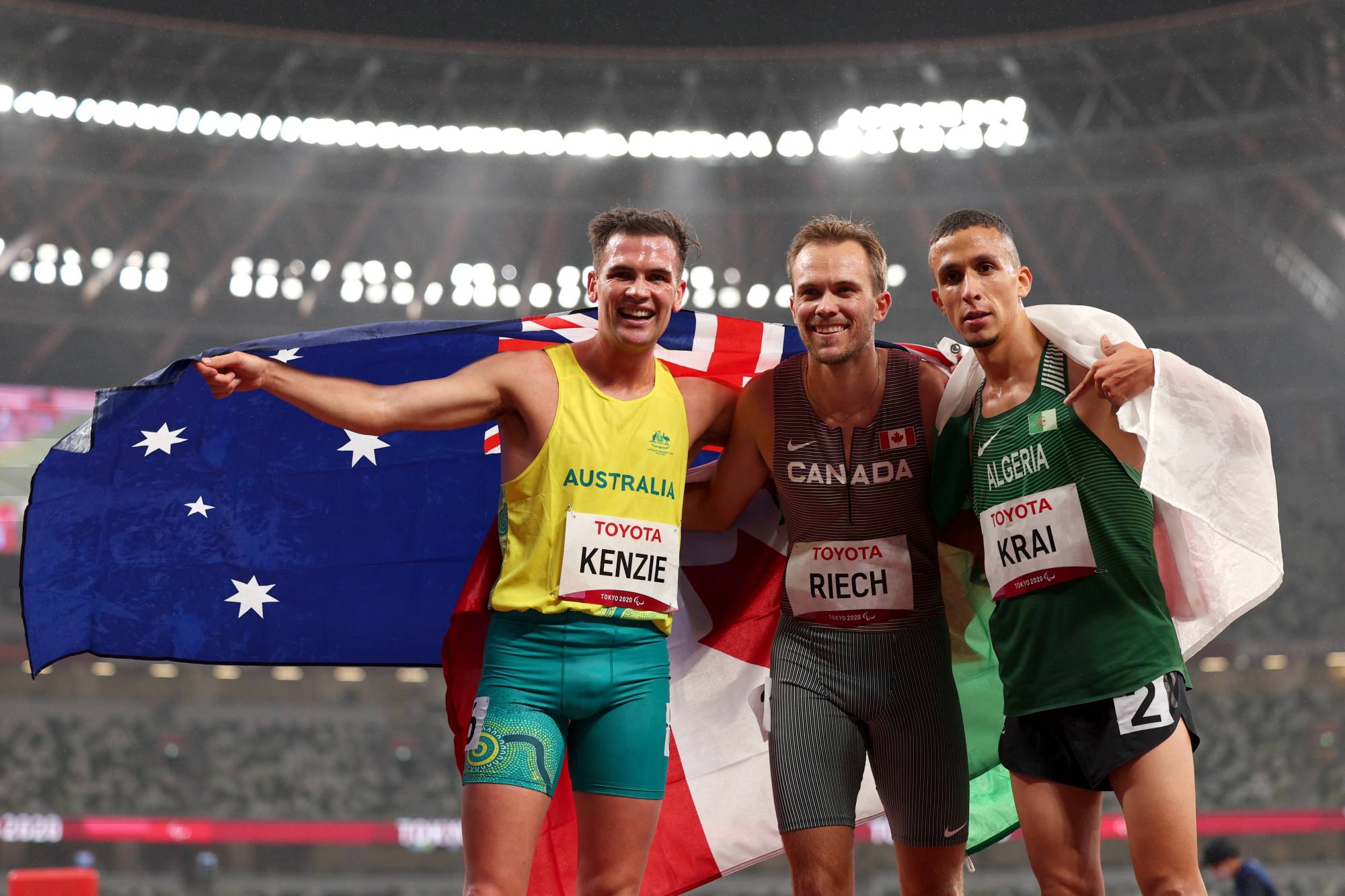 Canada's Nate Riech (center) celebrates after winning gold and setting a new Paralympic record in the men's T38 1,500 meters, along with silver medalist Abdelkrim Krai of Algeria (right) and bronze medalist Deon Kenzie of Australia. | REUTERS