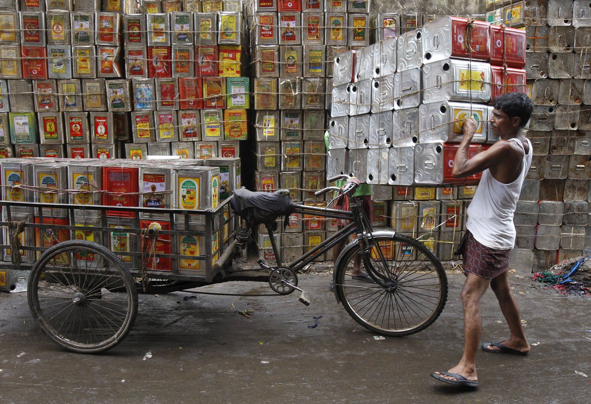 A man loads empty containers of edible oil onto a tricycle in Kolkata. | Reuters