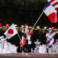 The French delegation\'s flag bearer enters the National Statdium ahead of Japan\'s flag bearer.  | KYODO