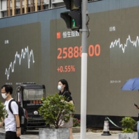 People walk past a screen displaying the Shenzhen Stock Exchange and the Hang Seng Index figures in Shanghai on Aug. 18. | BLOOMBERG