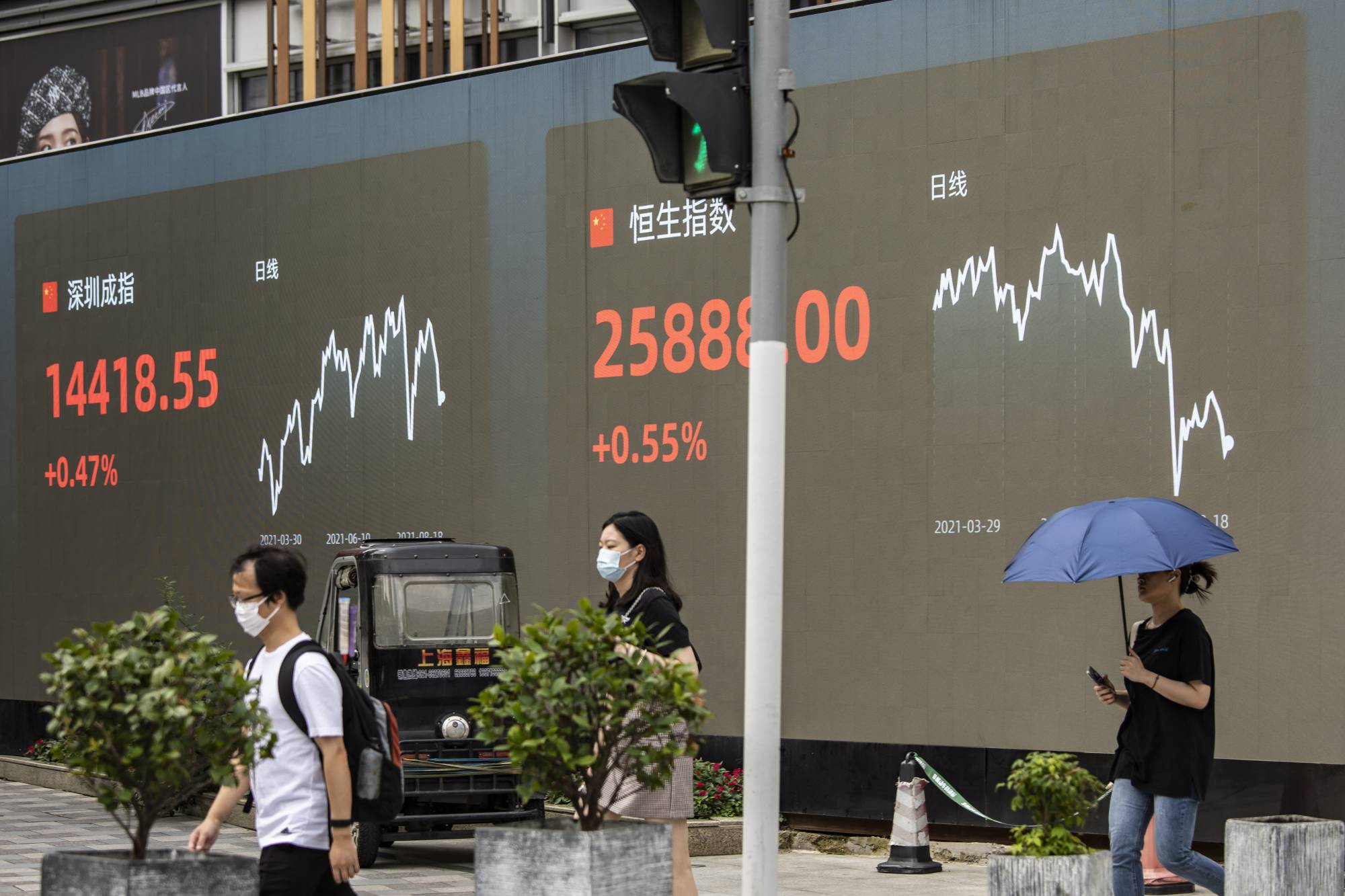 People walk past a screen displaying the Shenzhen Stock Exchange and the Hang Seng Index figures in Shanghai on Aug. 18. | Bloomberg