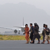 Taliban fighters walk past a Qatar Airways aircraft preparing to take off from the airport in Kabul on Thursday.  | AFP-JIJI