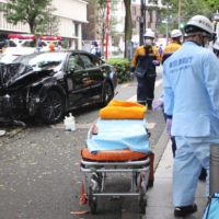 Paramedics attend an injured person, with a taxi that caused a deadly accident seen behind in Tokyo on Saturday. | KYODO