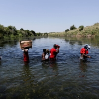 Asylum-seekers walk through the Rio Grande river on Sunday to cross the border between Ciudad Acuna, Mexico, and Del Rio, Texas.  | REUTERS 