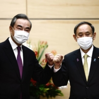 Prime Minister Yoshihide Suga bumps elbows with Chinese Foreign Minister Wang Yi at the start of their meeting in Tokyo last November. | POOL / VIA REUTERS