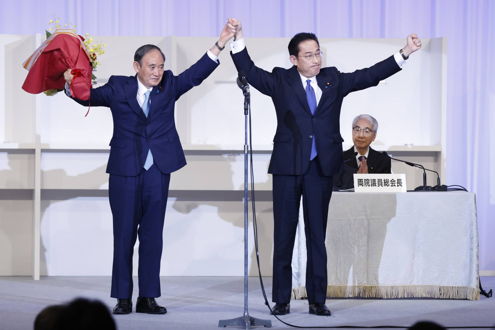 Fumio Kishida joins hands on stage with outgoing Prime Minister Yoshihide Suga after winning the ruling Liberal Democratic Party's leadership election on Wednesday in Tokyo. | Bloomberg