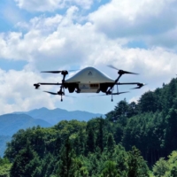 Aeronext Inc.\'s drone flies over the mountains around Kosuge Village in Yamanashi Prefecture. The company hopes drone deliveries will solve the last-mile logistical conundrum many rural communities in Japan are facing. | COURTESY OF AERONEXT INC.
