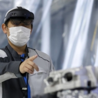 An employee wearing mixed reality goggles demonstrates the intelligent operation support system at Nissan Motor Co.\'s plant in Kaminokawa, Tochigi Prefecture, on Thursday. | BLOOMBERG