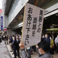 A man holds up a sign in Tokyo\'s Shinjuku Ward on Tuesday asking people to conduct social distancing while listening to candidates\' speeches as campaigning for the Lower House election kicked off. | KYODO