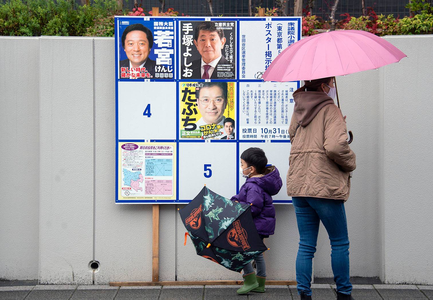 A boy and his mother browse local candidates on an election board outside a polling station as Japan's general election gets underway in Setagaya Ward on Sunday afternoon. | ROB GILHOOLY