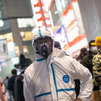 \"Fujiwara,\" 62, dressed in a Tyvek suit and mask, says he had come prepared to \"do battle with coronavirus and radiation\" but had chosen not to take on the polling booths. \"I feel I can make a bigger statement here,\" he says. | ROB GILHOOLY