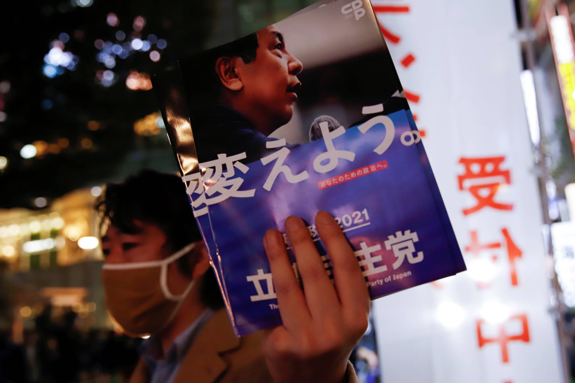 A man distributes the party leaflets before Yukio Edano, the leader of the Constitutional Democratic Party of Japan, speaks to voters on Saturday, a day before voting for the Lower House election, near Shinjuku Station in Tokyo. | REUTERS