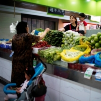 Two grandmothers with their granddaughters trade vegetables at a market on the outskirts of Shanghai. | REUTERS