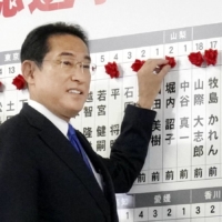 Prime Minister Fumio Kishida places a rosette above the name of a winner in the House of Representatives election on Sunday night in Tokyo. | KYODO