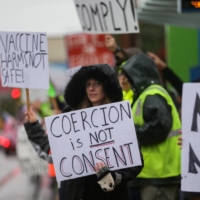 A woman holds a sign as Boeing employees and others protest the company\'s coronavirus vaccine mandate, outside the company\'s facility in Everett, Washington, on Oct. 15. | REUTERS