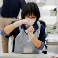 A laboratory technician puts chopped beef from cattle bred in Fukushima into a plastic container while preparing it for cesium testing at Fukushima Agricultural Technology Center. | REUTERS