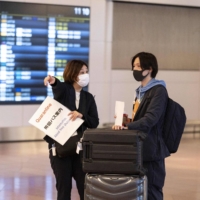 A passenger arriving from overseas is welcomed by a quarantine agent at the arrivals hall of Haneda Airport in Tokyo on Monday, after Japan eased border rules to allow students and business travelers amid the pandemic. | AFP-JIJI
