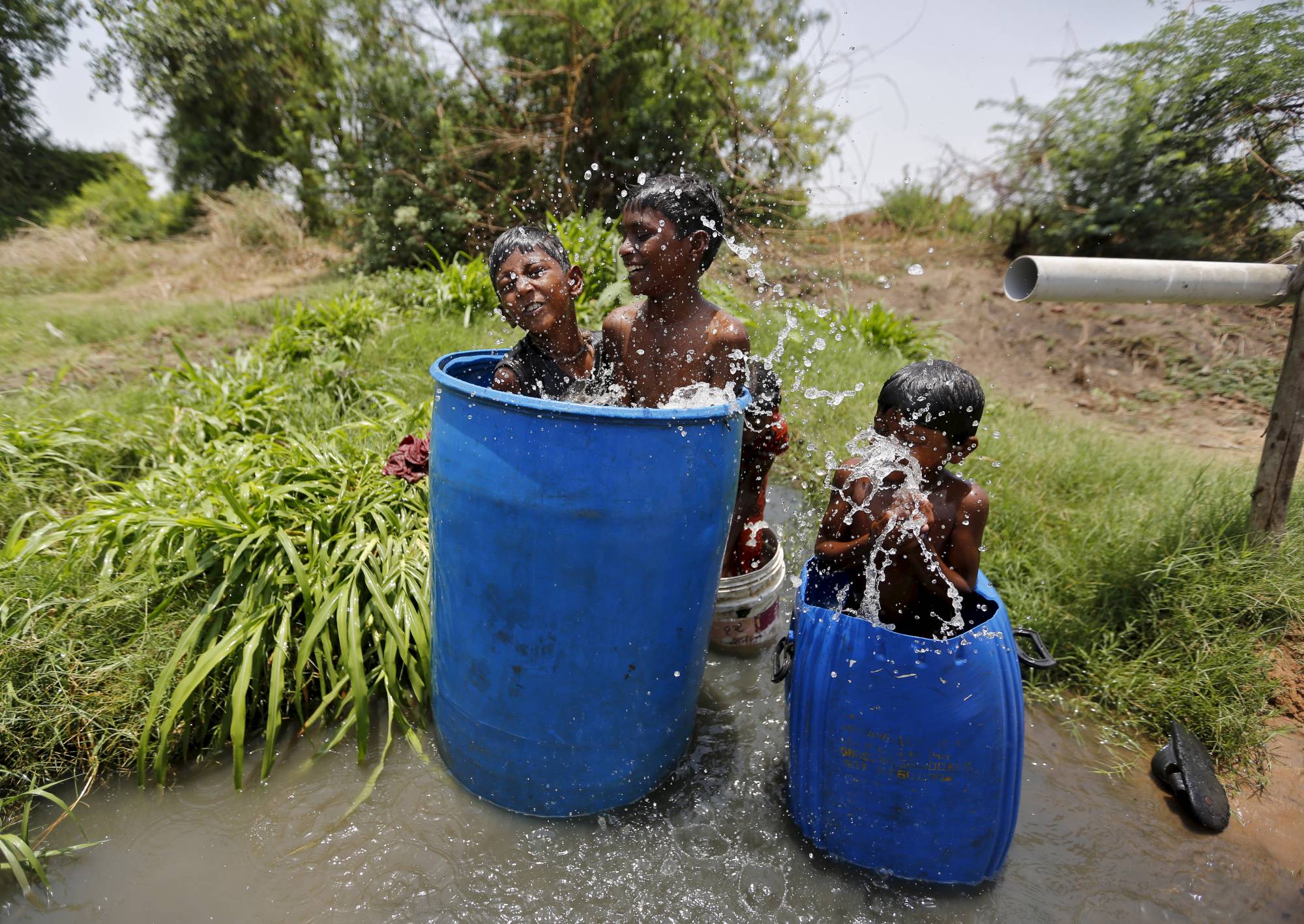 Children sit in containers filled with water as they cool themselves on a hot summer day on the outskirts of Ahmedabad, India. | Reuters 